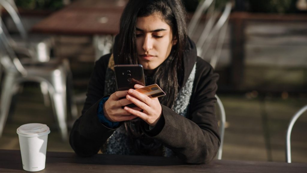 Una ragazza con una carta di credito e uno smartphone, che forse sta effettuando una transazione online